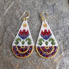 a pair of beaded earrings sitting on top of a stone surface with beads in the shape of tears