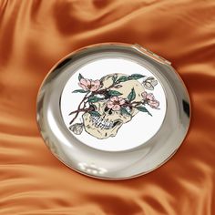 a plate with a skull and flowers painted on the front is laying on a satin surface