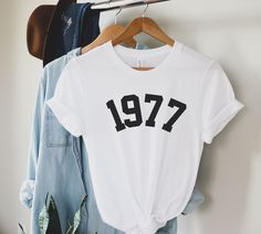 two t - shirts hanging on a clothes rack next to a plant and jacket hanger