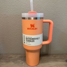 an orange tumbler cup with a straw in it sitting on a wooden table next to a wall