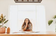 a woman sitting at a desk in front of a window with her hand on her chin