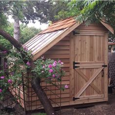 a small wooden shed with flowers growing around it