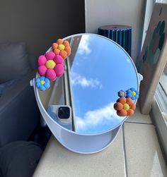 a round mirror sitting on top of a counter next to a couch and window sill