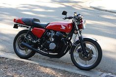 a red and black motorcycle parked on the side of the road next to a tree