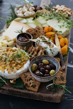 an assortment of cheeses, olives and crackers on a wooden platter