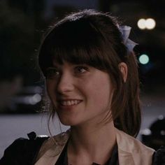 a young woman with bangs and a bow in her hair smiles at the camera while standing outside