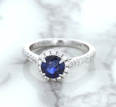 One of a kind round blue sapphire center surrounded by a sparkling diamond halo The perfect pop of color for when you decide to pop the question It's the perfect way to pop the question! A ring made for a princess - this gorgeous setting features a royal blue sapphire surrounded by a halo of sparkling diamonds. We love how dainty and feminine this ring is. It is a modern twist on the classic engagement ring. Perfect for the modern bride. It can serve both "something new and something blue" on yo Dazzling Blue Round Diamond Ring, Dazzling Round Sapphire Ring With Halo Setting, Blue Halo Ring In 14k White Gold, Lab-created Sapphire Halo Ring With Brilliant Cut, Dazzling Blue Sapphire Ring With Halo Setting, Blue Sapphire Halo Ring With Brilliant Cut, Sapphire Halo Ring With Lab-created Gemstone, Sapphire Halo Ring With Gemstone, Sapphire Gemstone Halo Ring