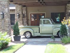 an old pick up truck parked in front of a house with potted plants on the driveway