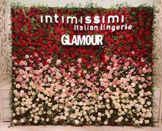 a flower wall with red and white flowers in front of the words, intimismi italian lingerere glamour