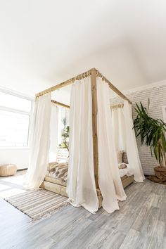 a white canopy bed sitting in a bedroom next to a potted plant