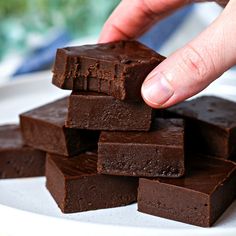 a hand is picking up some brownies on a plate