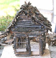 a small house made out of branches and logs sitting on top of a wooden block