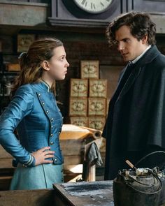 a man and woman standing next to each other in front of a desk with a clock on the wall