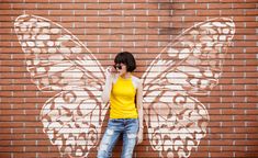 a woman standing in front of a brick wall with a butterfly painted on it