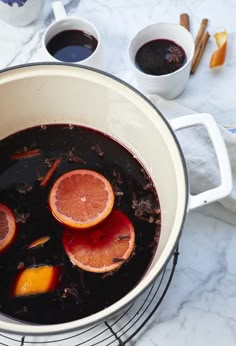 a pot filled with blood oranges on top of a counter next to two cups of coffee