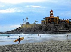 people are walking on the beach with surfboards and buildings in the backgroud