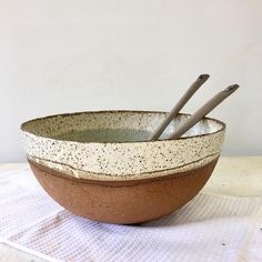 two brown and white bowls with spoons in them on a tablecloth next to a wall