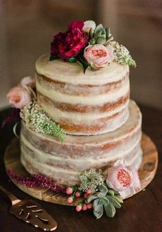 a three tiered cake with flowers and greenery sits on a wooden platter