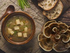 a bowl of soup with tofu and mushrooms next to bread on a wooden table