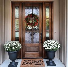 two large planters with flowers sit on the front porch next to a welcome mat