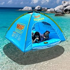 a blue tent sitting on top of a sandy beach next to the ocean with people in it