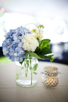 blue and white flowers in a glass vase on a table next to a beaded jar