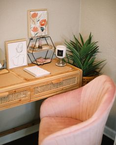 a pink chair sitting in front of a desk with pictures and a potted plant