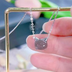 a hand holding a tiny cat necklace in front of a metal bar with a chain attached to it