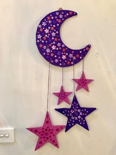 three stars hanging from the side of a purple and pink moon with flowers on it