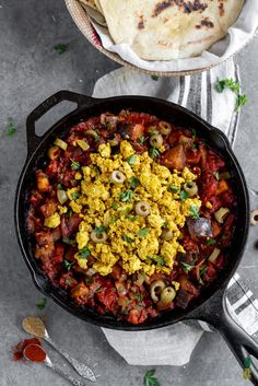 an iron skillet with eggs and vegetables in it next to a tortilla