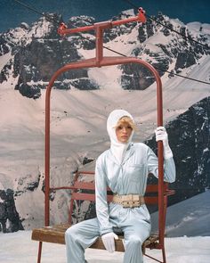 a woman sitting on a ski lift in front of a snow covered mountain with mountains behind her