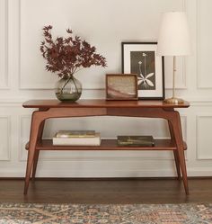 a wooden table topped with a vase filled with flowers next to a lamp and framed pictures