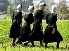 four women in black dresses are walking through the grass