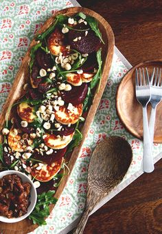 a wooden platter filled with lots of food on top of a table next to a fork and spoon