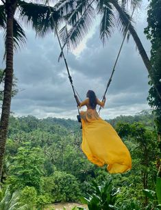 a woman in a yellow dress is swinging on a rope between two palm trees and the jungle