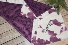 two purple and white bandanas with black letters on them, sitting next to a pine tree