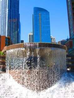 a large fountain in the middle of a city with skyscrapers in the back ground