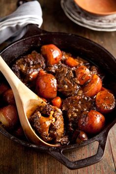 a skillet filled with meat and potatoes on top of a wooden table