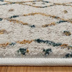 a white rug with green, yellow and blue designs on the bottom is laying on a wooden floor