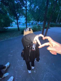 two people standing in the middle of a road with their hands making a heart shape