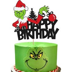 a green cake topped with a happy birthday topper and an angry grino face