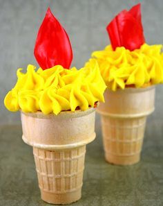 two ice cream cones with yellow and red frosting on them, one is shaped like a flower