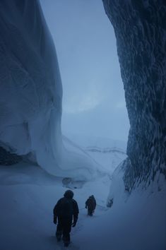 two people walking up a snow covered mountain in front of an ice cave on a foggy day