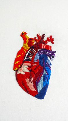 an embroidered heart is shown on a piece of white paper with red, yellow and blue colors