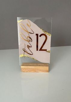 a white and gold table number sitting on top of a wooden block with a wood base