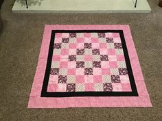 a pink and black patchwork quilt on the floor in front of a chair with flowers