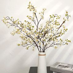 a white vase filled with flowers sitting on top of a table next to a stack of books