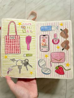 a hand holding an open notebook with stickers on the pages and various items in it