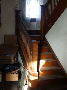 sunlight shining through the window onto an old wooden staircase with boxes on the ground below