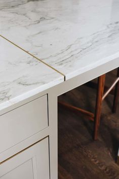 a white marble counter top with gold lines on the edge and two wooden chairs behind it